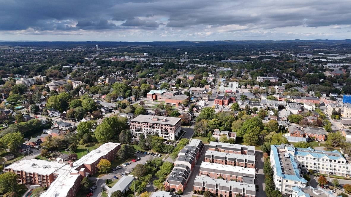 Aerial view over Cobourg’s rooftops and tree-lined streets toward the hills